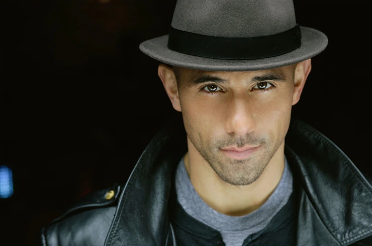 Billy Dec in a close-up editorial-style portrait wearing a fedora and dark leather jacket