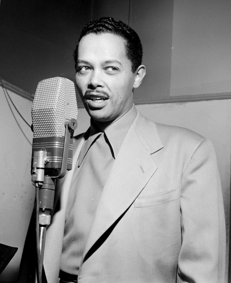 Black-and-white portrait of jazz singer and bandleader Billy Eckstine standing beside a studio microphone.