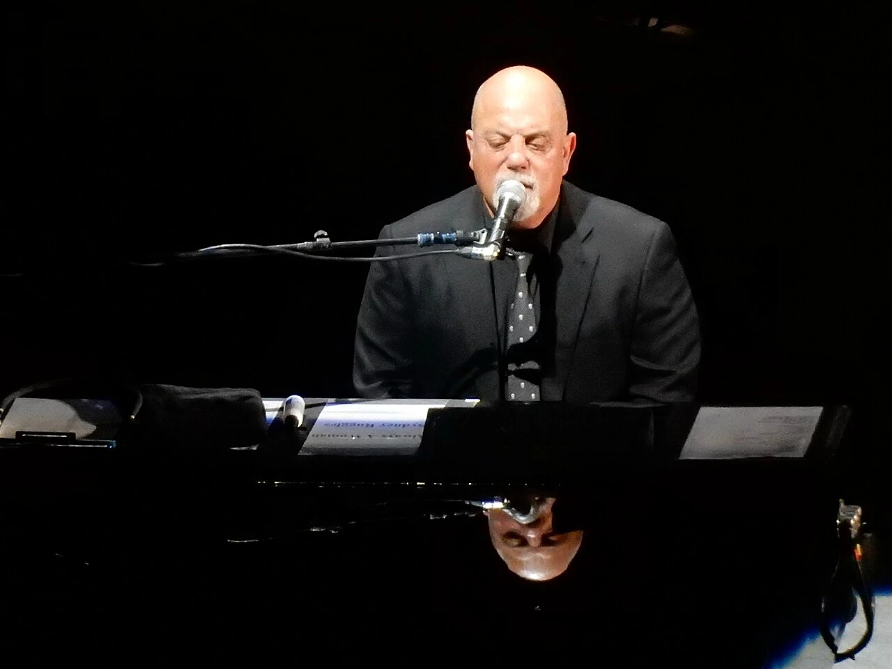 Billy Joel performing at a piano and microphone on stage